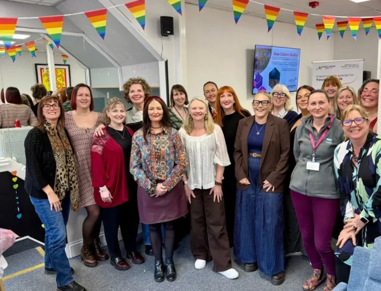 A large group of women gathered under rainbow bunting at a Proud and Diverse Cumbria event