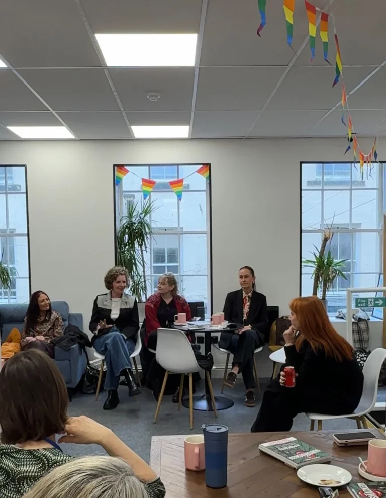 People sitting and talking at a gathering in a room decorated with rainbow bunting