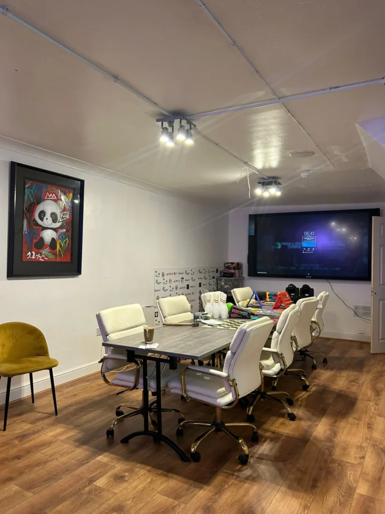 Meeting room with a long table, white chairs and a wall screen
